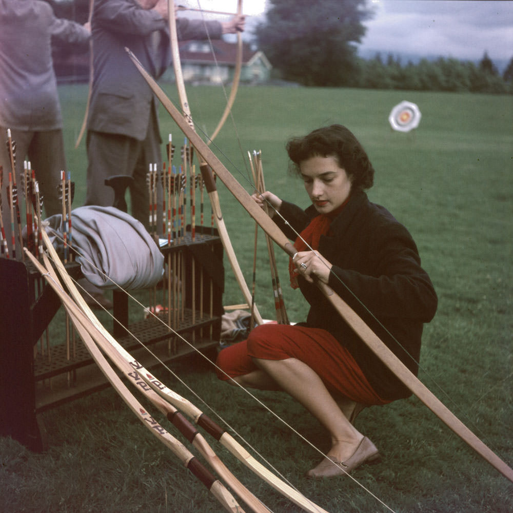 #18 Woman kneeling with bow and arrow in her hands. Archery in Stanley Park, 1954