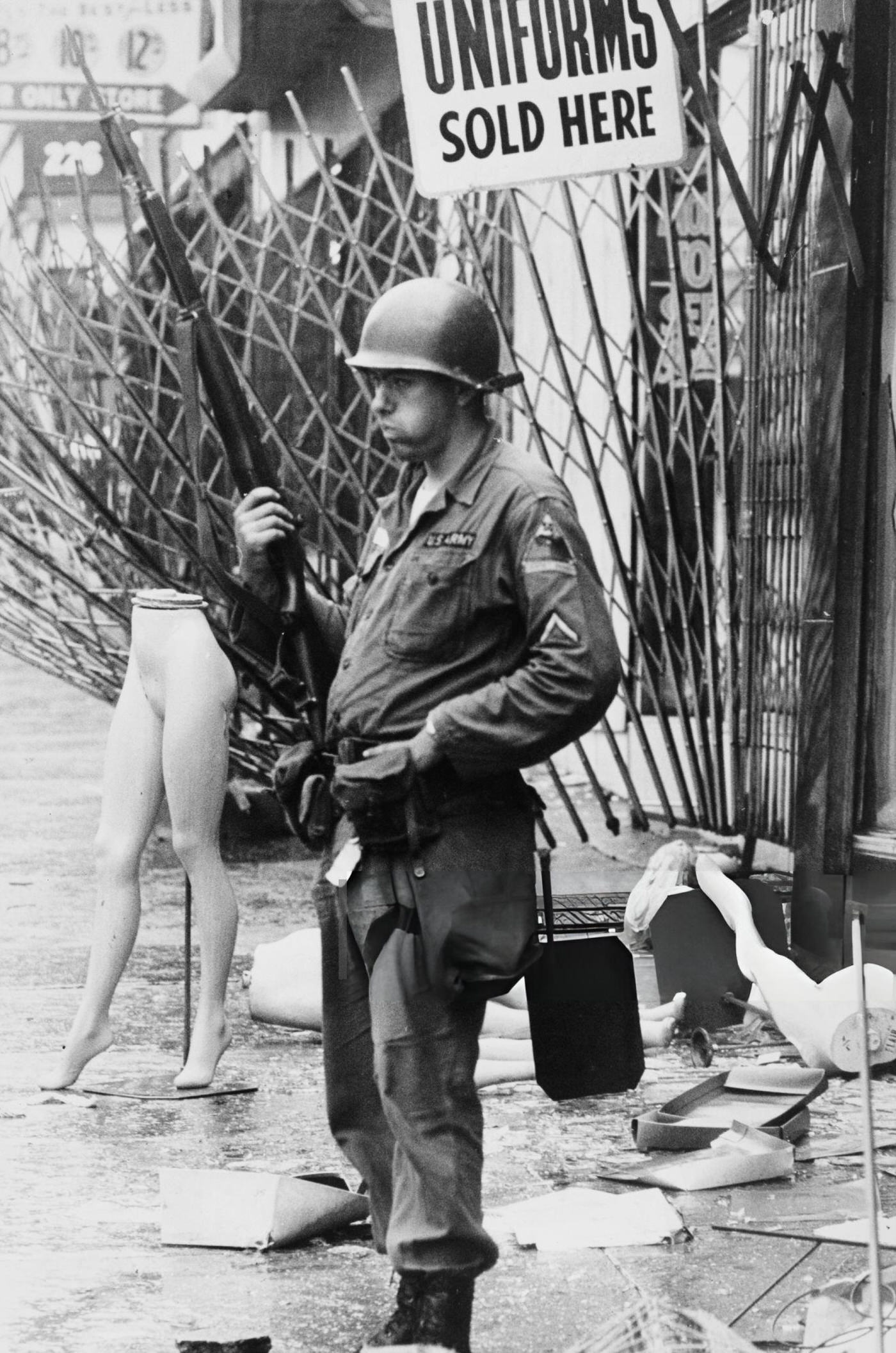 #14 A soldier of the National Guard stands next to a mannequin’s legs and a sign reading ‘Uniforms Sold Here’