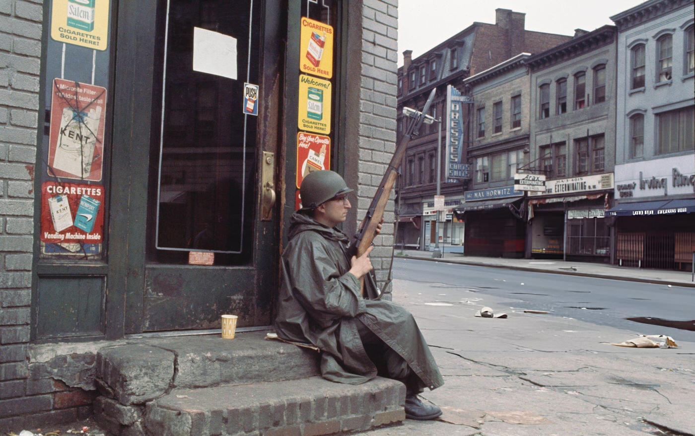 #42 A member of the National Guard sits with his rifle on the steps of a closed convenience store