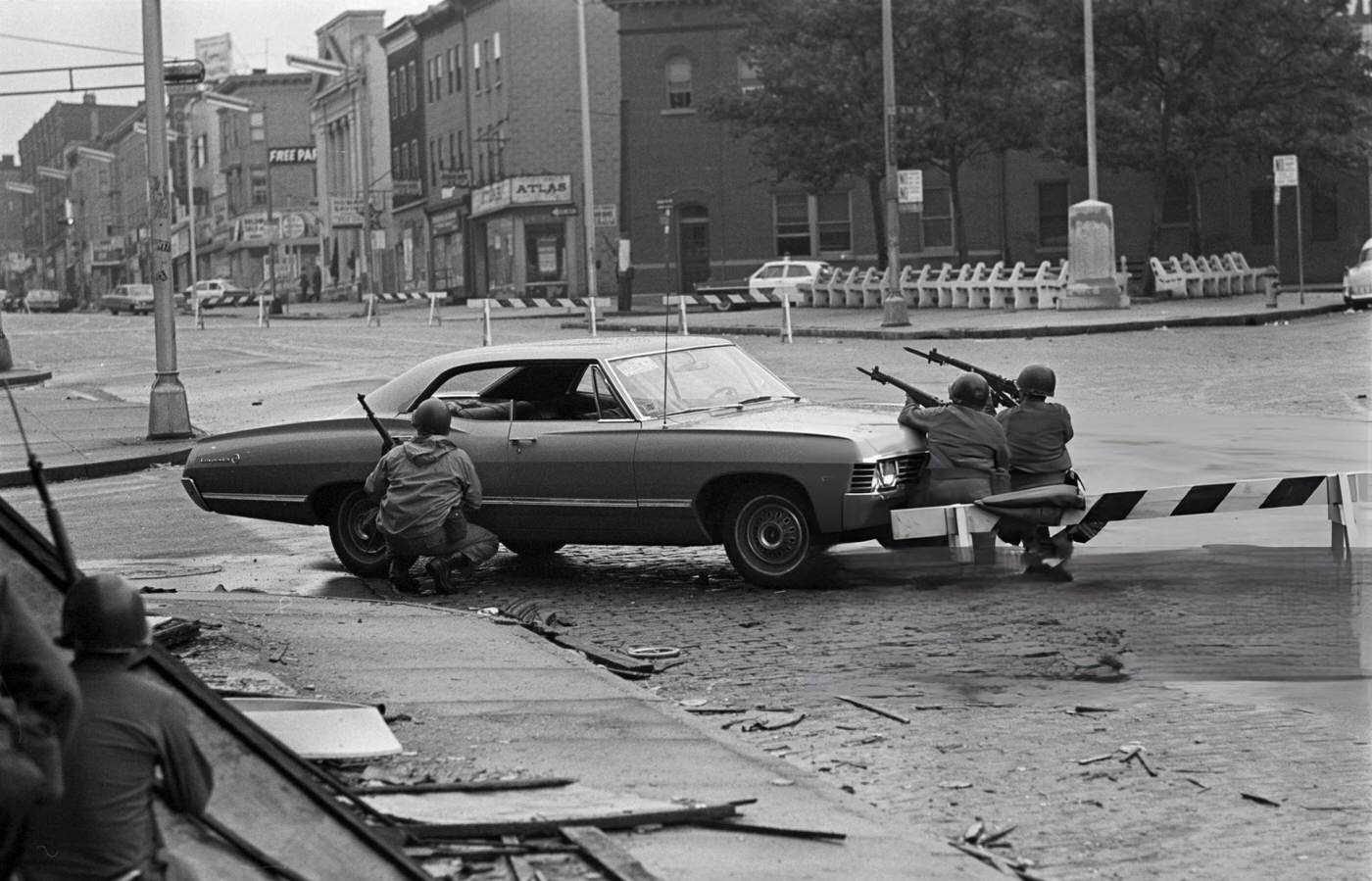 #46 National Guard soldiers taking cover behind a car, guns pointed towards the street