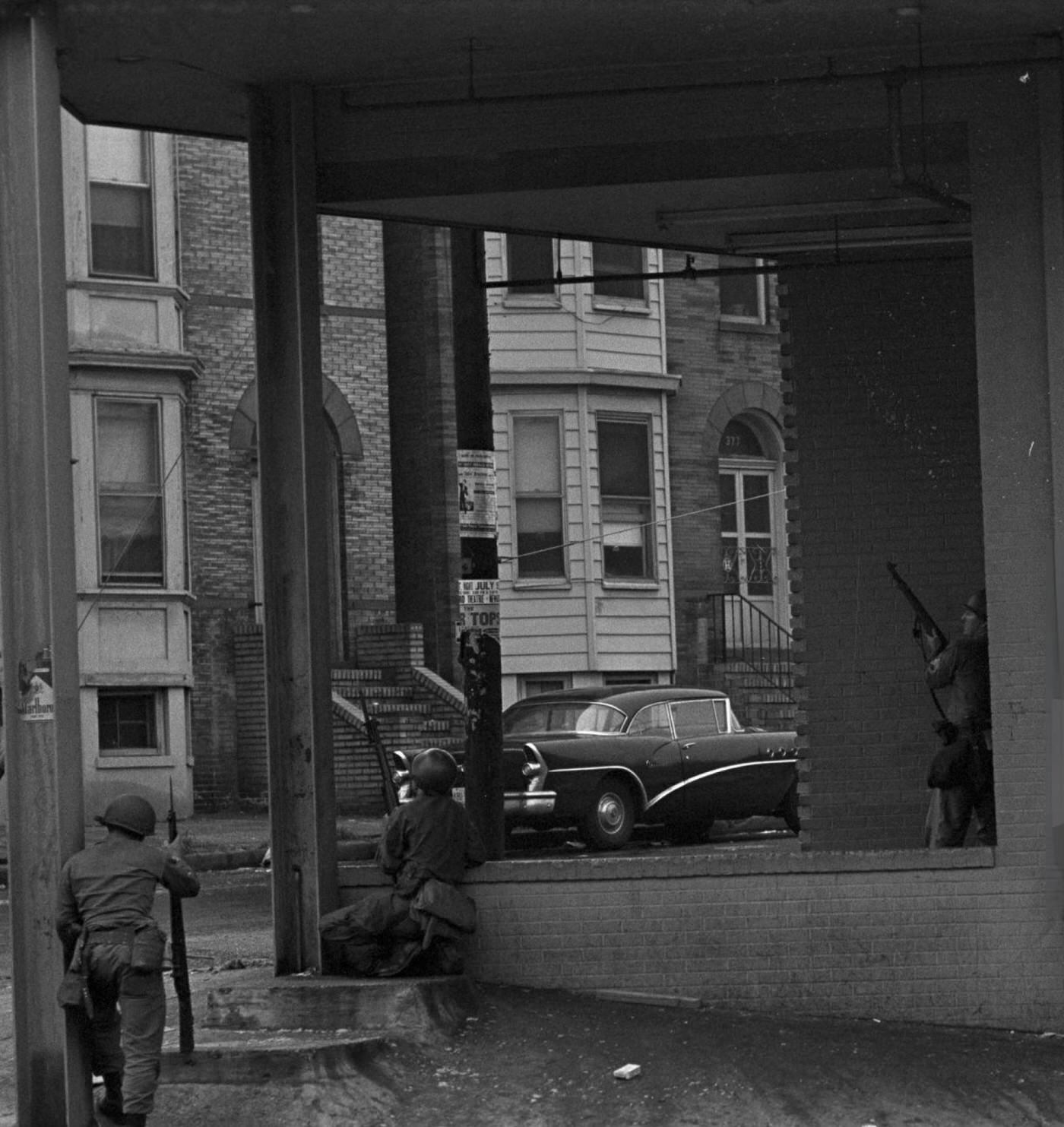 #48 National Guard soldiers taking cover under the awning of a building, guns pointed towards the street