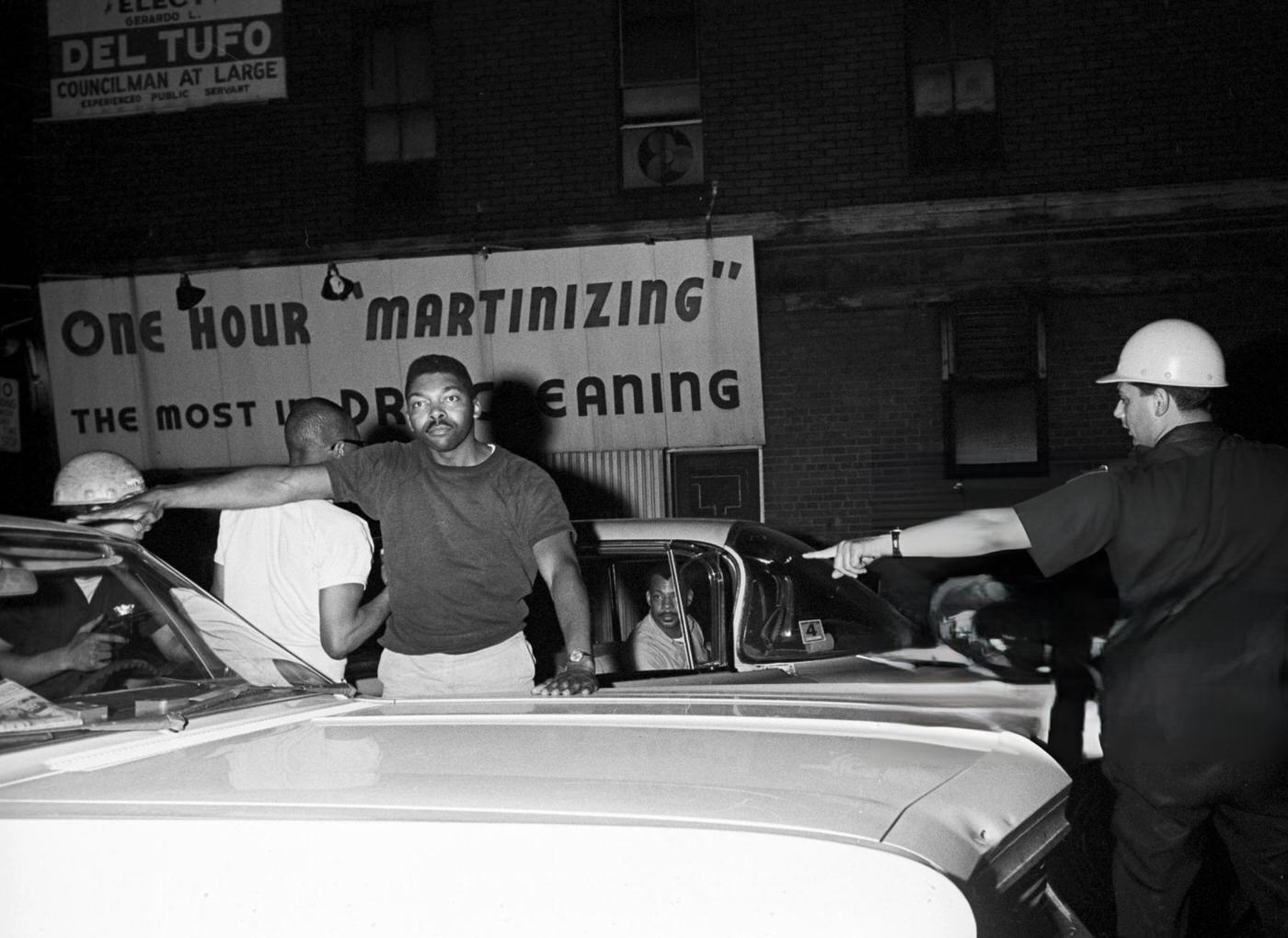 #55 A National Police officer searches an African American man in front of a parked car