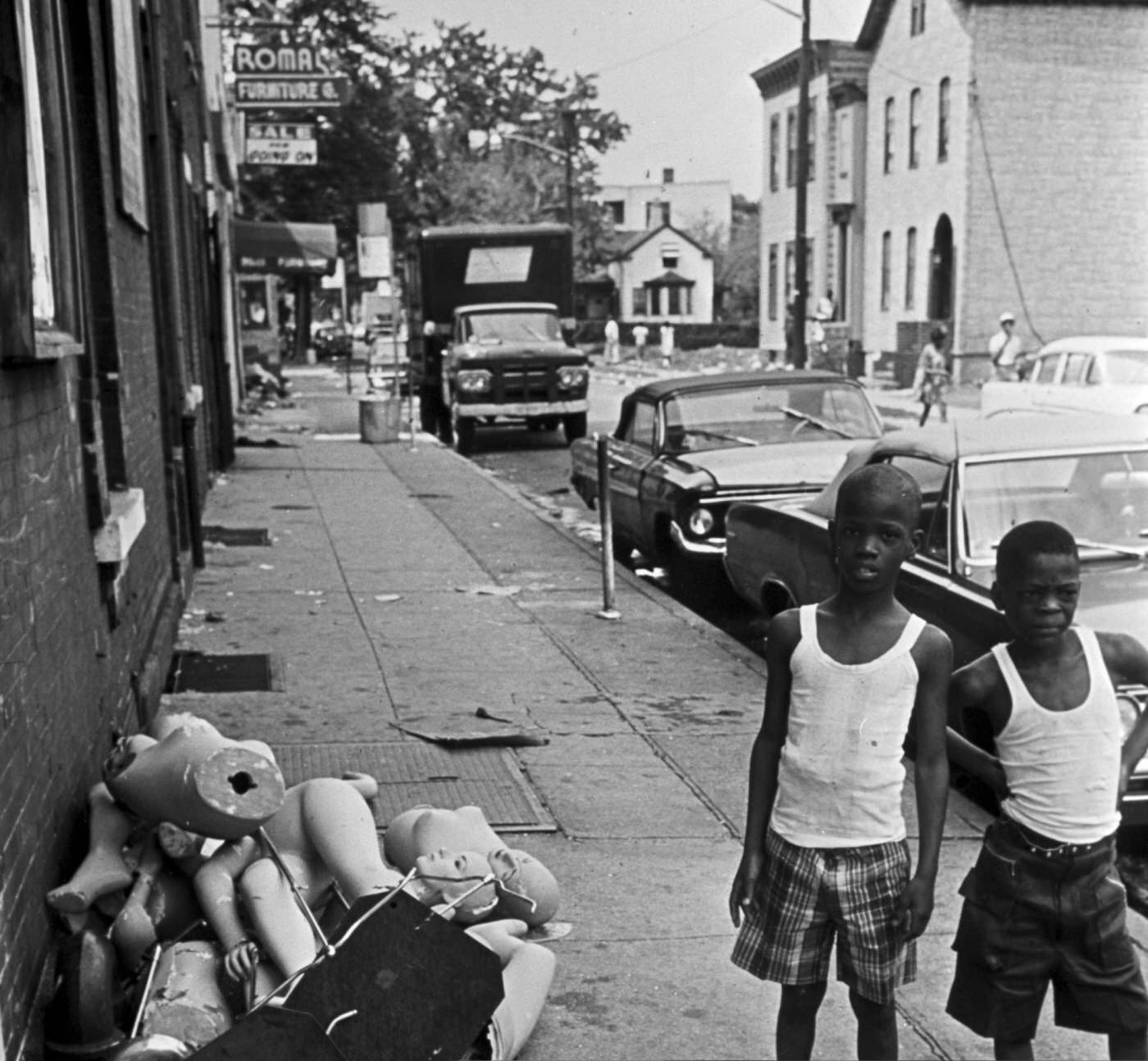 #74 Two young African American boys in t-shirts and Bermuda shorts near broken mannequin busts on the sidewalk