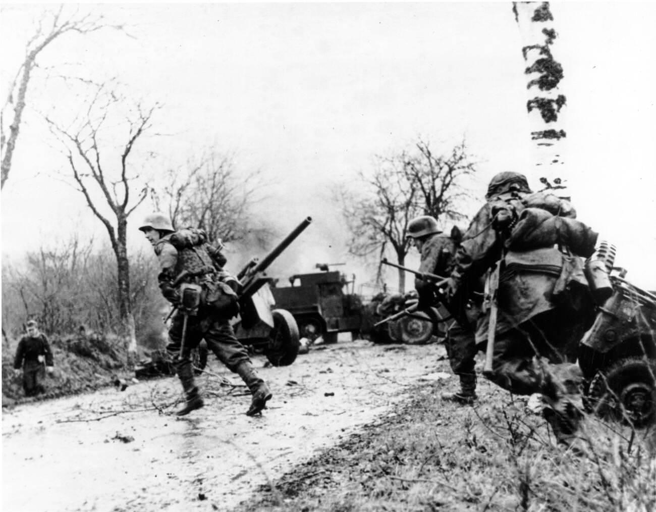 #20 German troops advancing past abandoned American equipment during the Battle of the Bulge, 1944.