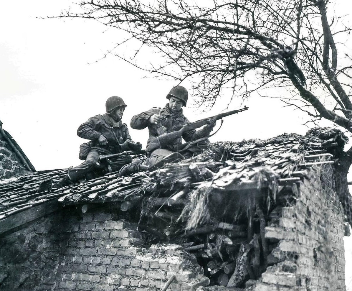 #30 S/Sgt. Urban Minicozzi and Pfc. Andy Masiero stop to reload while sniping snipers from the roof of a building in Beffe, Belgium, 1945.