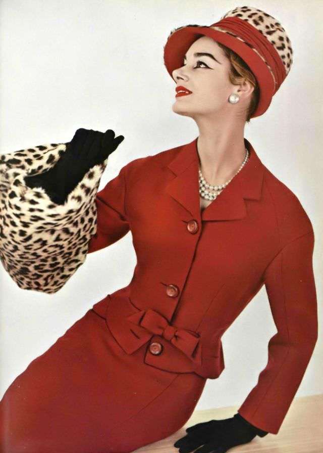 #15 Jacky Mazel in a red Shetland wool suit, the fitted jacket has a small bow at the waist, worn with a leopard fur muff and hat by Pierre Balmain, 1956.