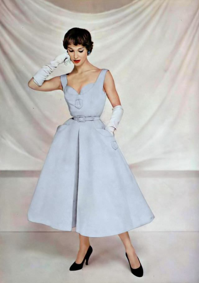 #8 Ann Farrar in a pale blue ottoman dress, the bodice has buttoned tabs as do the pockets, the skirt is wide with an inverted pleat, by Pierre Balmain, 1954.