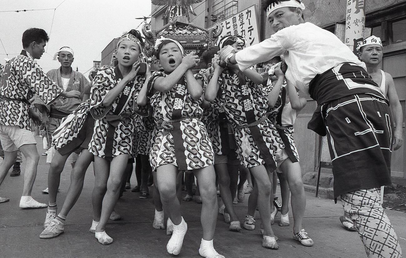 #29 Boys in happy coats heave a mikoshi, a portable Shinto shrine, at a matsuri in Tengenji, Tokyo, 1958.