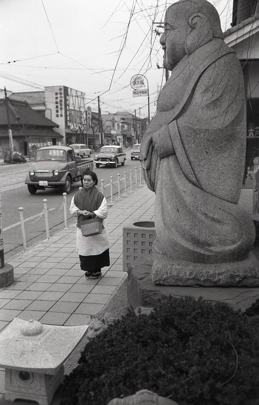 #31 A housewife carrying a shopping bag walking in front of a statue of Ebisu at Tengenji, Tokyo, 1957.