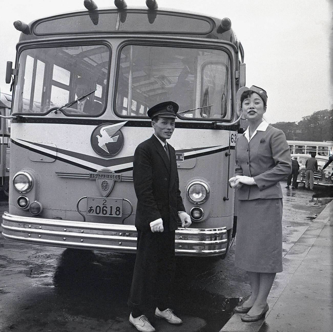 #61 Uniformed male and female guides stand outside a parked up Isuzu tourist bus, 1950s.