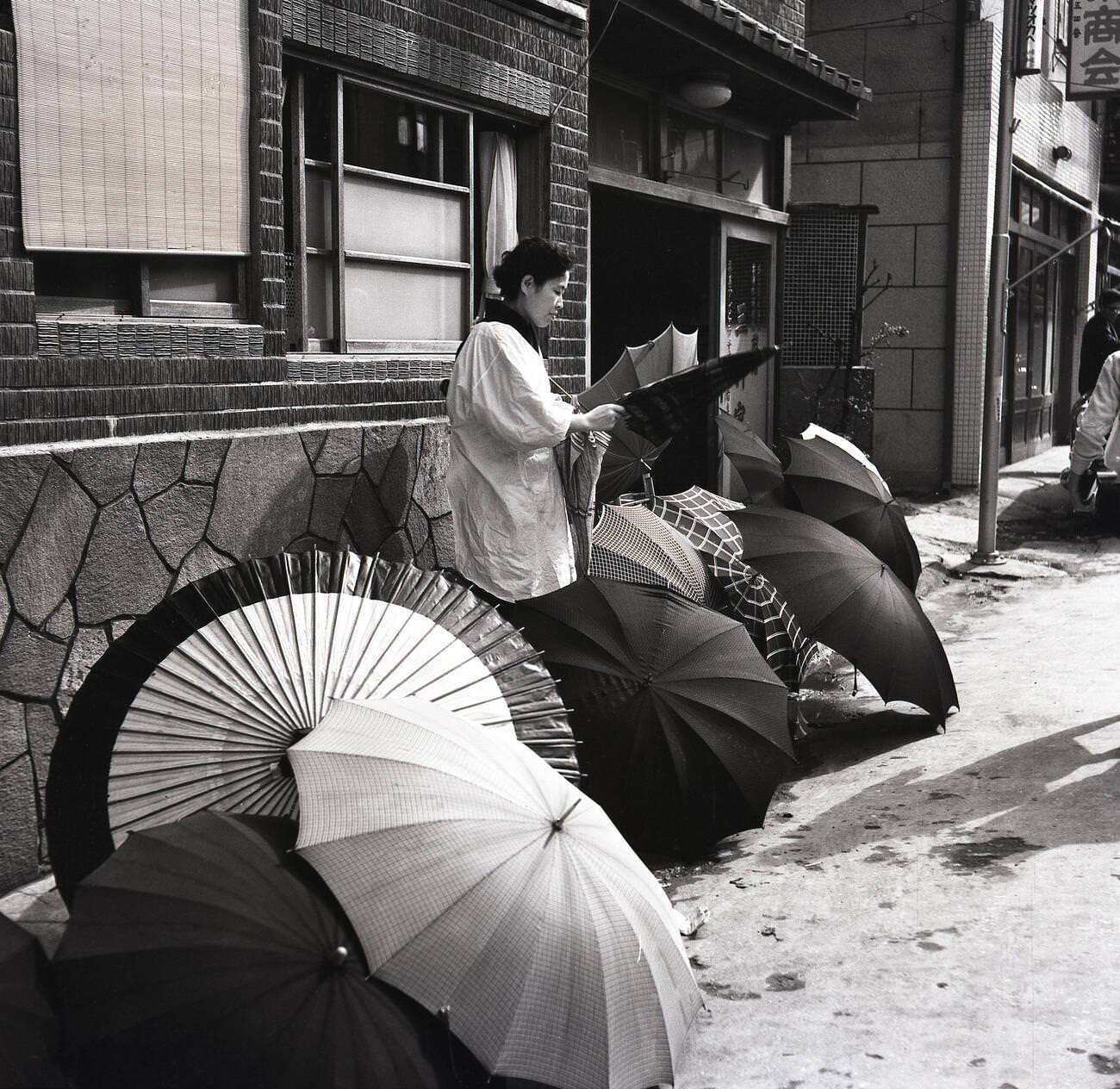 #86 A female Japanese street trader outside a building selling umbrellas in Tokyo, 1950s.