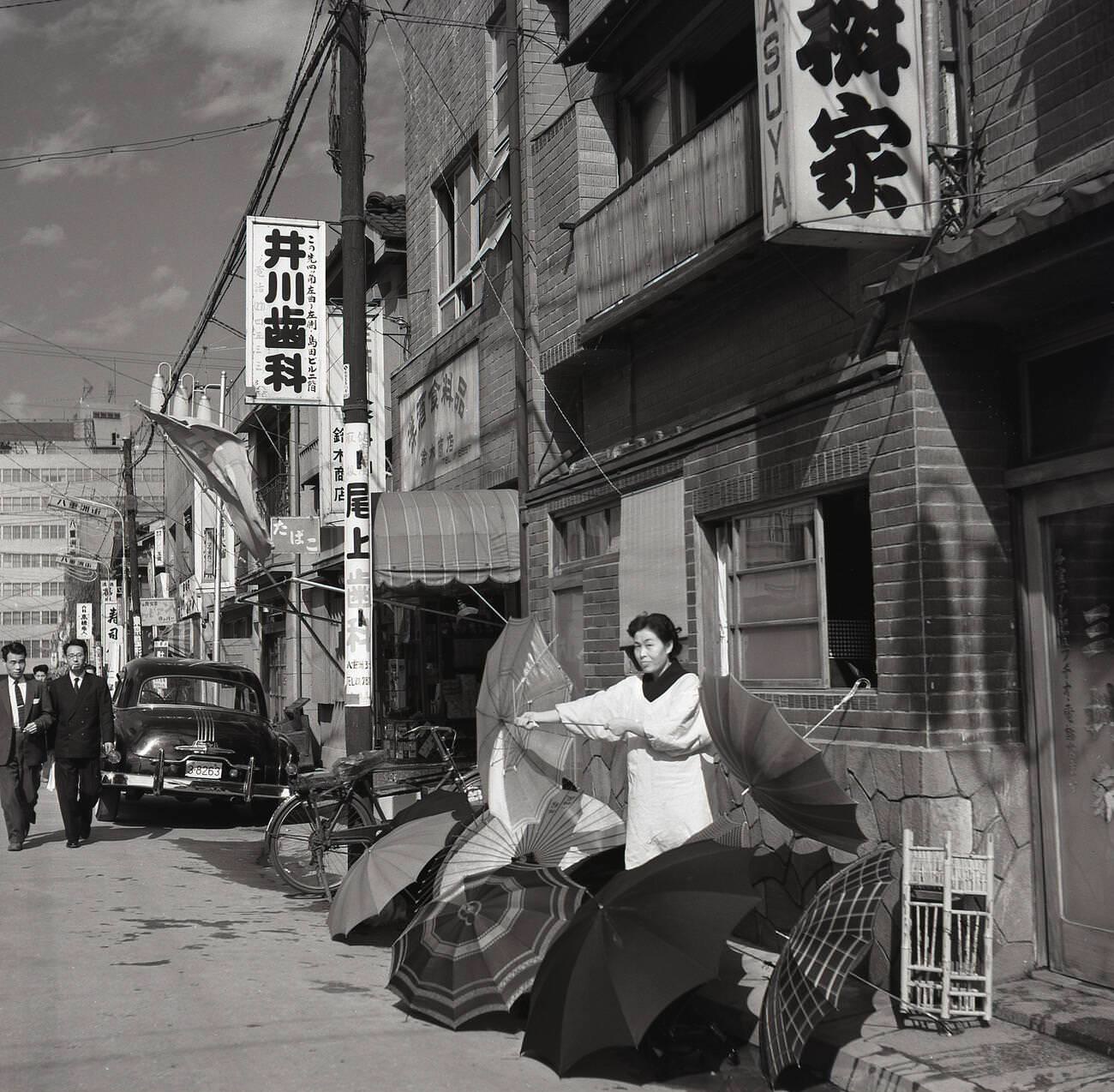 #87 A female Japanese street trader outside a building in the old town selling umbrellas in Tokyo, 1950s.