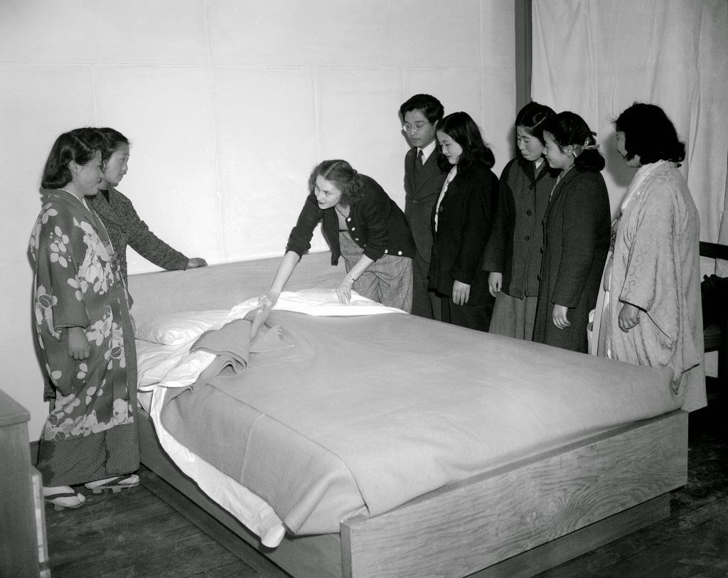#100 Although given preliminary instructions the girls are a bit vague about the proper making of a bed. Mrs. Anderson, with the help of an interpreter attached to the liaison section for the housing development, demonstrates the American way of bed making in Tokyo, 1947.