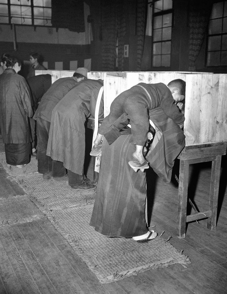 #62 A Japanese woman carries her son on her back as she marks her ballot in Tokyo, 1946.