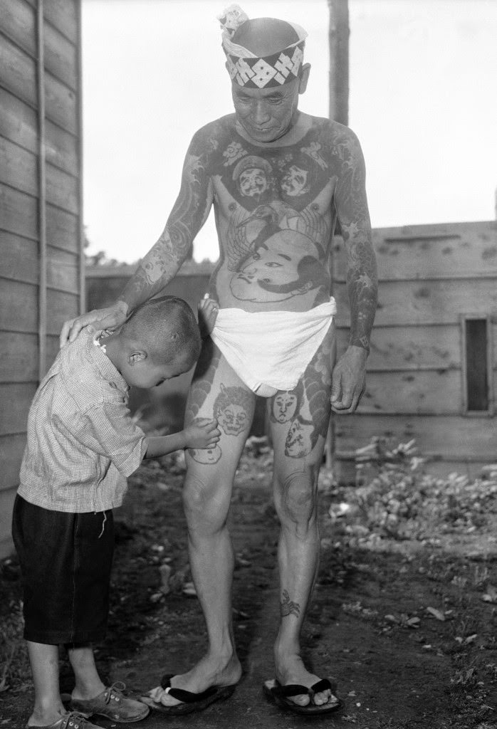 #87 At the “Hard Skin Club” convention of tattooed men and women in Tokyo, a little boy examines a design on his father’s leg, 1948.