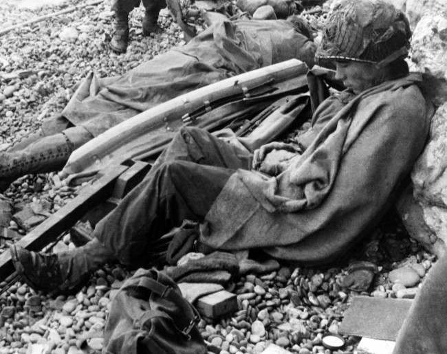 #19 Two American soldiers rest against a chalk cliff on the beach of the Normandy coast of France, 1944.