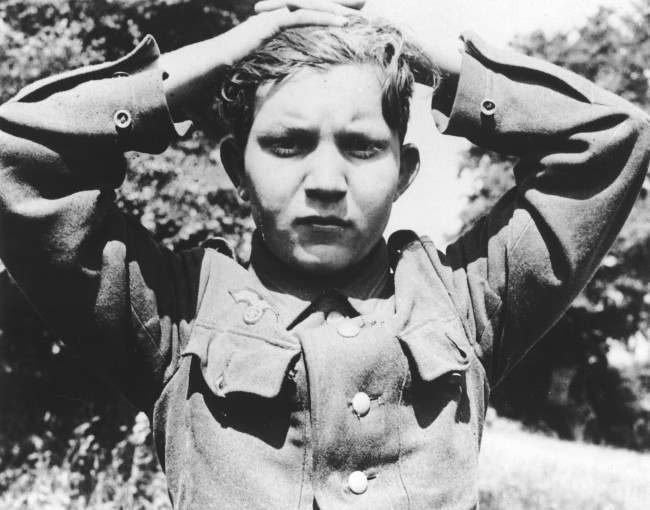 #22 A 16-year old German soldier has his hands clasped over his head as he is taken prisoner, 1944.