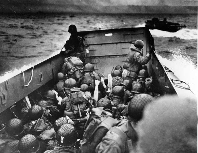 #29 A U.S. Coast Guard landing barge, tightly packed with helmeted soldiers, approaches the shore at Normandy, France, 1944.
