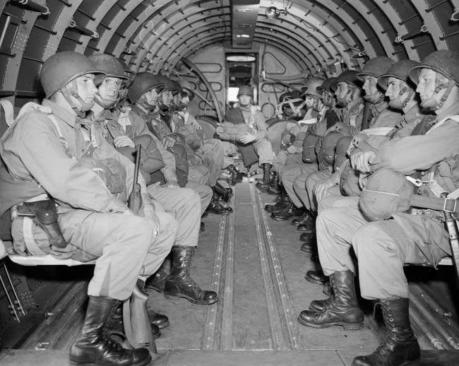 #42 American paratroopers, heavily armed, sit inside a military plane as they soar over the English Channel en route to the Normandy French coast, 1944.