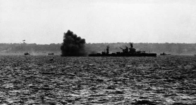 #47 A puff of black smoke blows away from the guns of the USS Arkansas as the might battleship lays down a tremendous barrage, 1944.