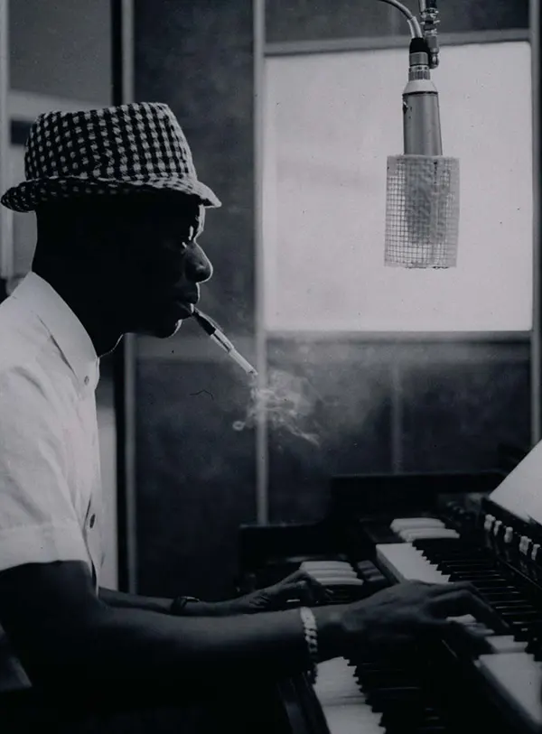 #30 Nat King Cole enjoys a smoke while he plays his tunes on a piano.
