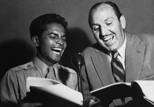 #29 Well known film star, Sabu, Staff Sergeant Sabu Dastagir, now serving as an aerial gunner attached to the 13th U.S. Air Force on active service in the Pacific, gets a laugh from Bob Dyer, radio comedian, as Sabu rehearses for a radio show, while on leave in Sydney, New South Wales on Feb. 27, 1945.