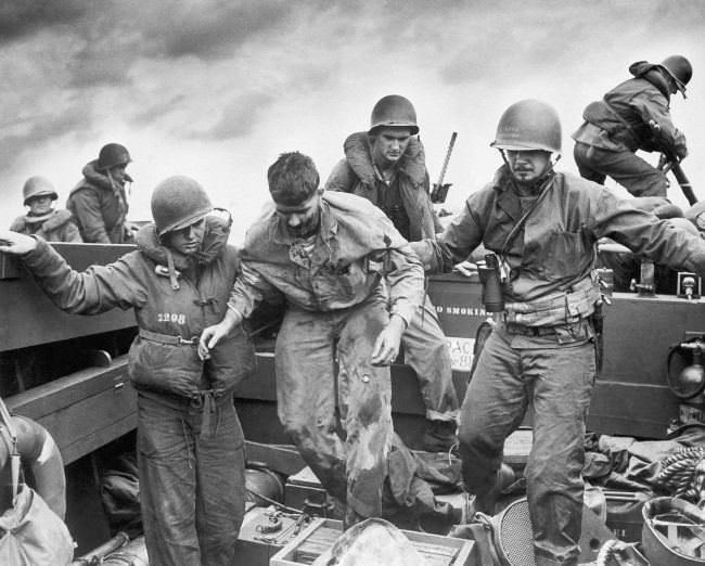 #21 Wounded when Jap fire made a direct hit on an Amtrac, a Marine is transferred by Coast Guardsmen to a landing craft off the flaming shore of Iwo Jima, Japan on D-Day, 1945.