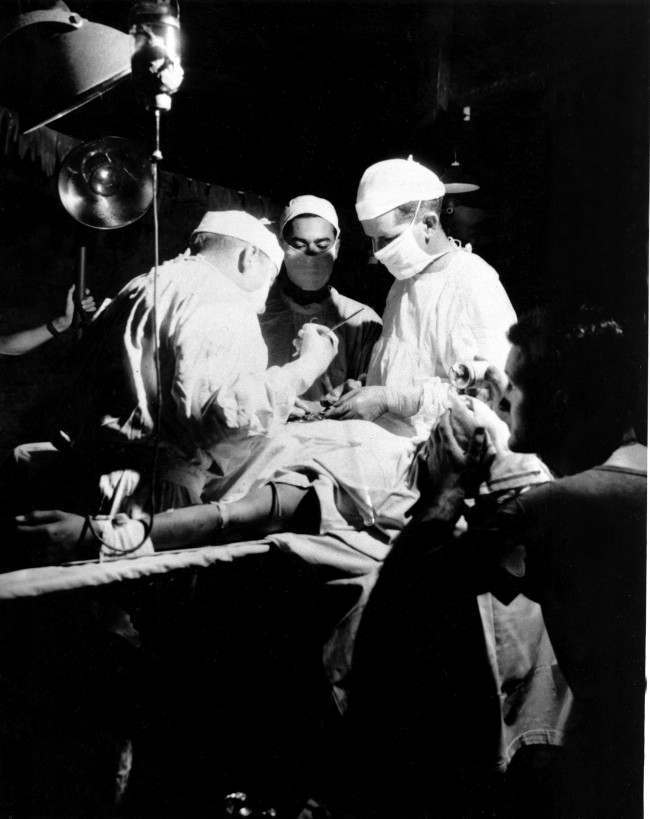 #34 While a U.S. corpsman administers ether, Navy doctors operate to remove shrapnel from the abdomen of a wounded leatherneck at the Fourth Marine Division evacuation hospital in Iwo Jima, Japan, 1945.