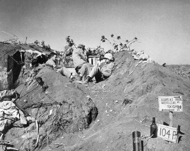 #38 U.S. Marines with a coast guard combat photographer found crouching in a listening post dug in Iwo Jima’s coffee grounds sands, Japan, 1945.