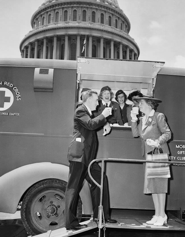 #19 Red Cross workers, demonstrating one of the five mobile canteen units acquired for relief work in the event Washington has an air raid, stop by the Capitol on June 18, 1942, and dish up mugs of coffee for Senator Joseph C. O’Mahoney, left, (D-Wyo.) and Rep. Edith Nourse Rogers, right, (R-Mass.).