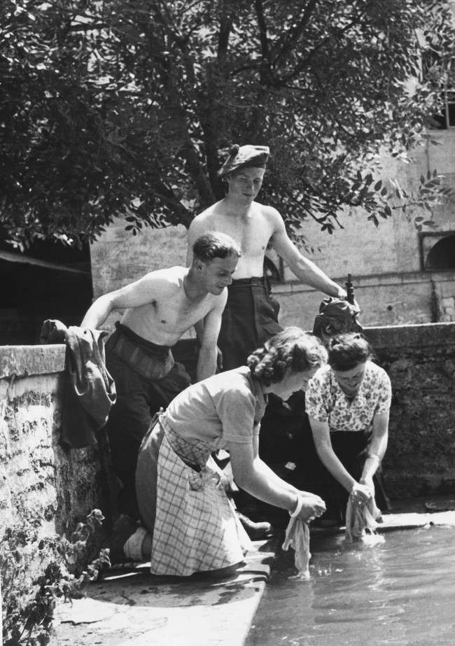 #16 Two British soldiers taking part in the liberation of France from the Germans are rewarded by Frenchwomen, of a Normandy farm, by having their laundry washed for them in France, 1944.