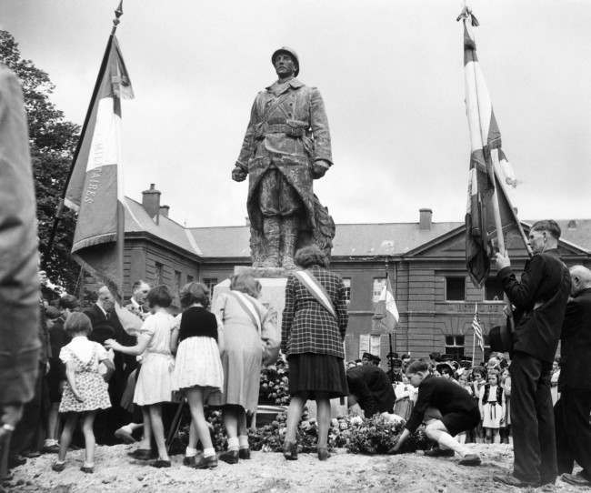 #18 Bastille Day celebrations in the little Normandy town of Isigny, 1944, took the form of services at the town’s War Memorial. French children pass in turn to lay their tributes to war dead at the War Memorial during the services.