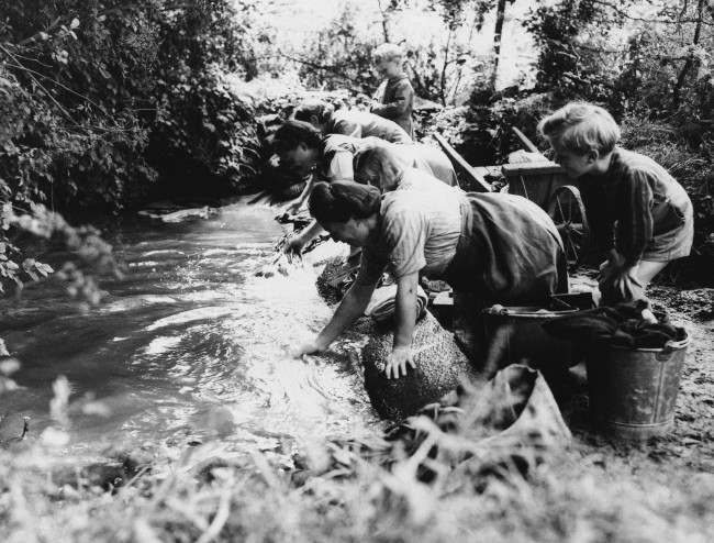 #8 French children watch their mothers wash clothes in a brook in Normandy, 1944, in an area liberated from the Nazis by American Forces.