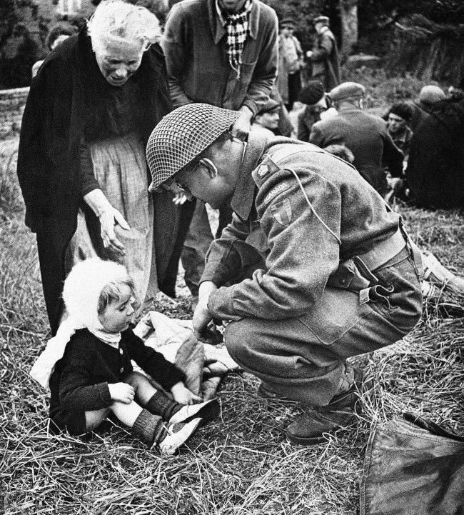 #22 A Canadian soldier, serving with the British forces in Normandy, France, strikes up an acquaintance with a little French girl, 1944, one of a group of refugees that were fed by the liberating armies. The feeding arrangements were organized by the Civil Affairs.