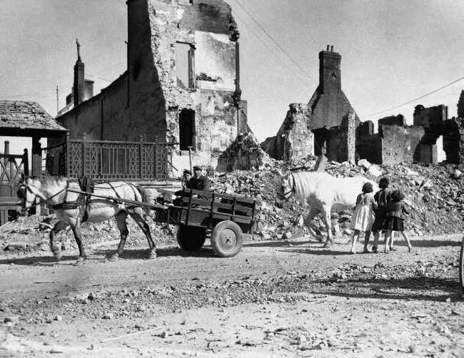 #27 Natives of a French village shattered by the Normandy invasion fighting move down a road past ruined buildings, 1944.
