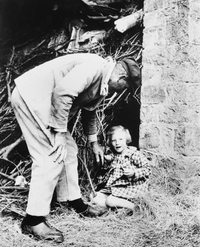 #28 A bright-eyed little French girl is persuaded to leave the spot, behind a pile of branches, where she made her home when the Allies swept into her community in Normandy, 1944.