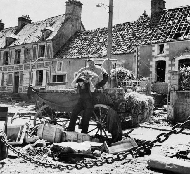 #39 Two French civilian refugees from the battle that raged in St. Sauveur as American troops advanced on Cherbourg, 1944, unload their cart after returning to their homes.