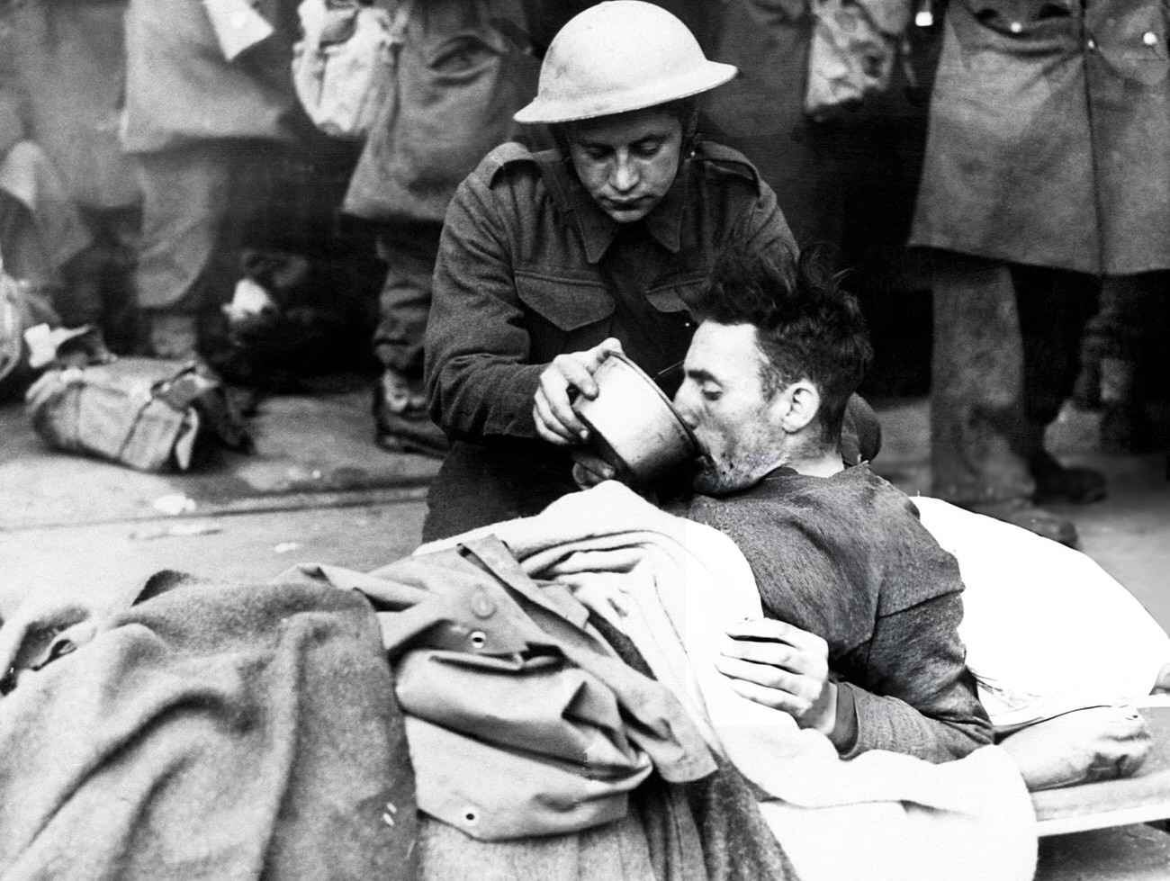 #42 A British soldier helps a wounded man drink while waiting to be evacuated from Dunkirk, France, 1940.