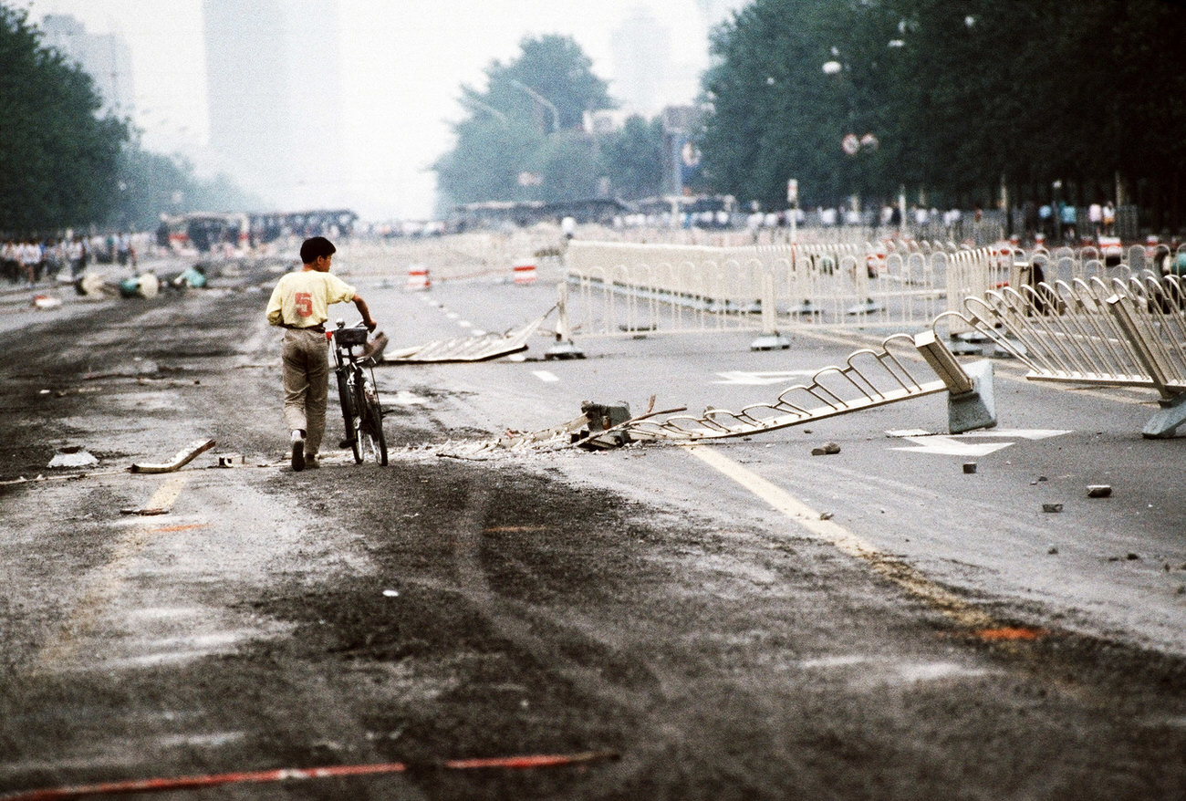 #25 A lone cyclist walks past street barriers on Changan Avenue that have been crushed by Chinese army tanks during the night of violence in and around Tiananmen Square.