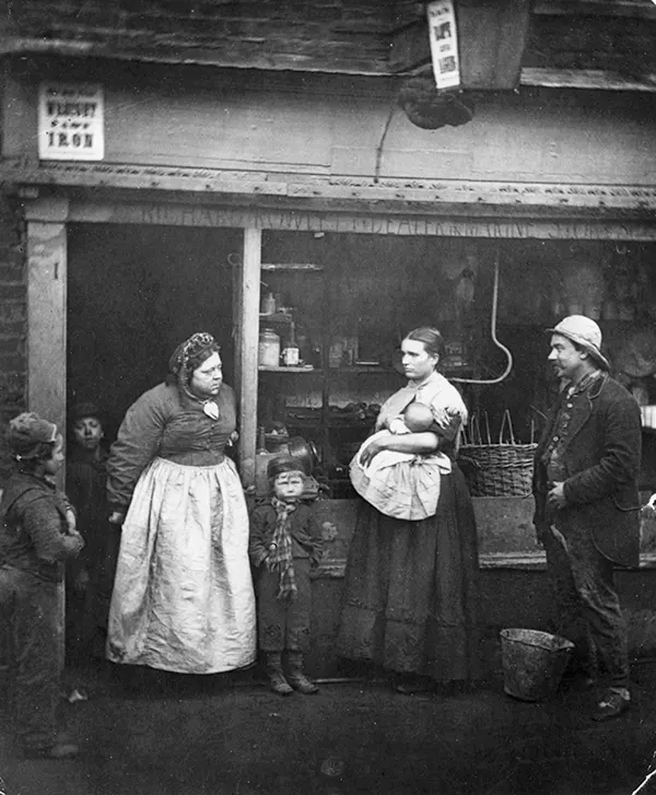 #20 In this 1877 photograph, Londoners affected by flooding stand in front of a rag shop.