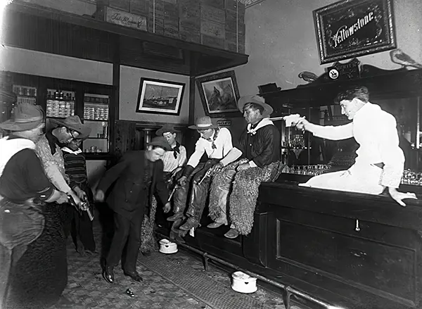 #12 At an unspecified saloon, possibly in Wyoming, patrons are seen apparently compelling a man to “dance” by pointing their guns at his feet, 1880s.