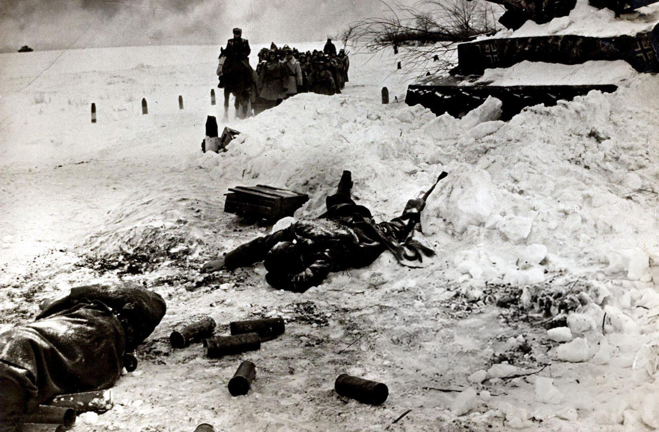 #14 A dead Russian soldier lies by a wrecked German tank as a troop of Russian soldiers pass during the battle of Stalingrad, 1942.