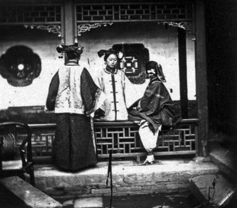 #15 In this 1868 photograph, three Chinese ladies gather for a chat in what looks like a courtyard. Chinese women’s clothing was considered unshapely and demure by Western standards, even at that time.