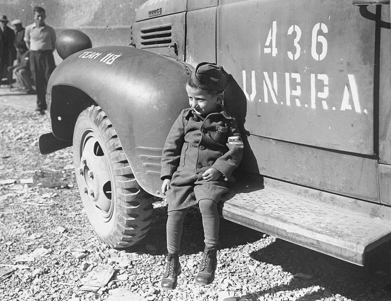 #12 A four-year-old survivor of Buchenwald sits on the running board of an UNRRA truck soon after the liberation of the camp. , 1945.