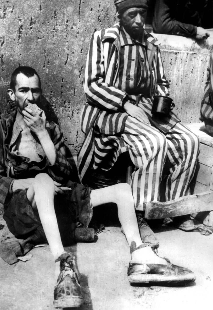 #14 Two emaciated former prisoners lean against a wall while eating a loaf of bread after the liberation of the Buchenwald concentration camp, 1945.