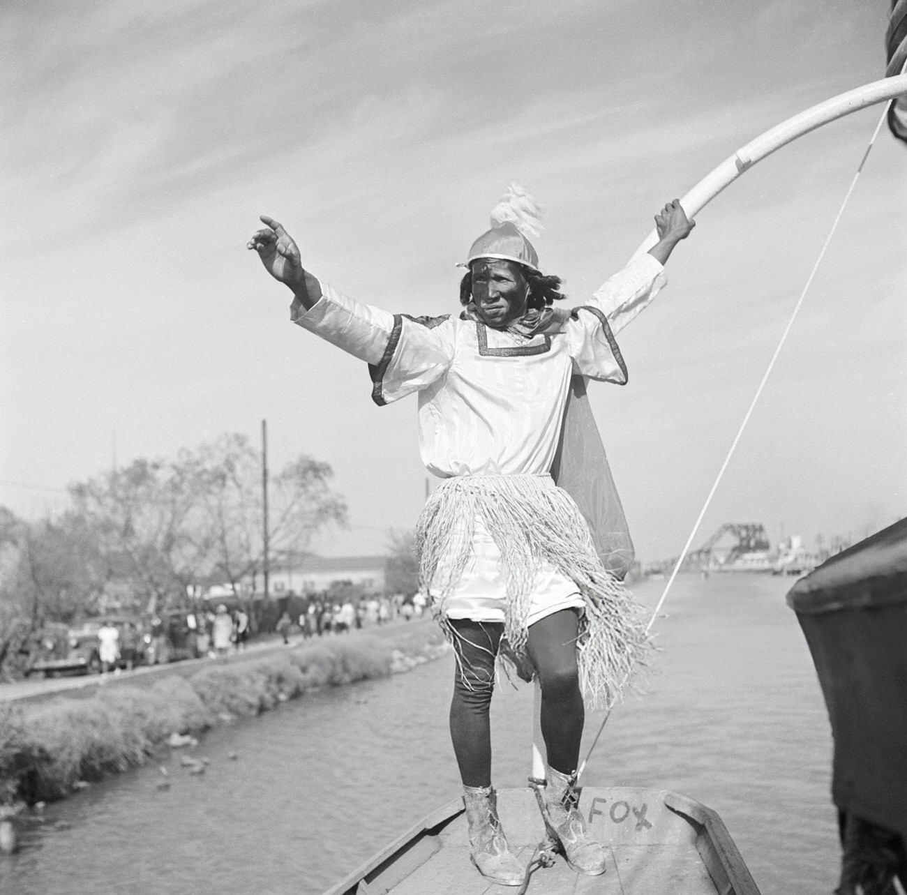 #30 A Man in a Mardi Gras Boat Parade on a Canal Wearing a Costume and Carrying a Longbow Dances, 1950s.