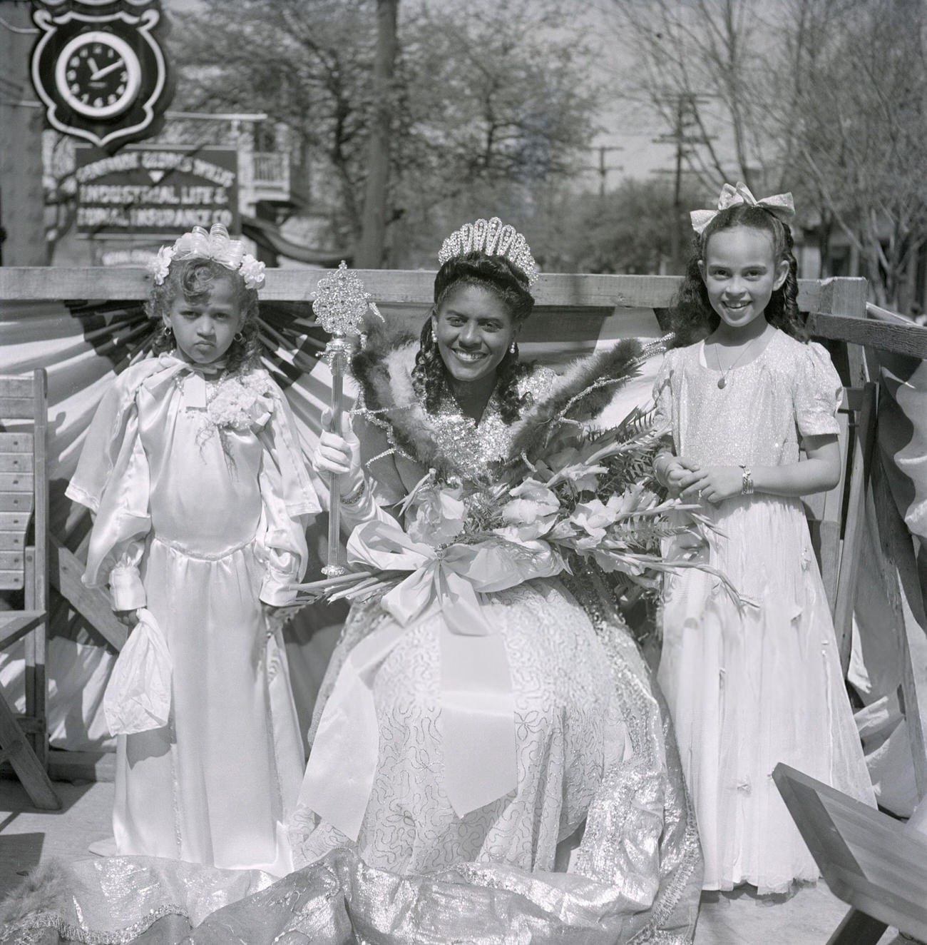 #41 A Mardi Gras Princess and Two Younger Attendants Ride a Parade Float Wearing White Gowns and Holding Bouquets, 1950s.