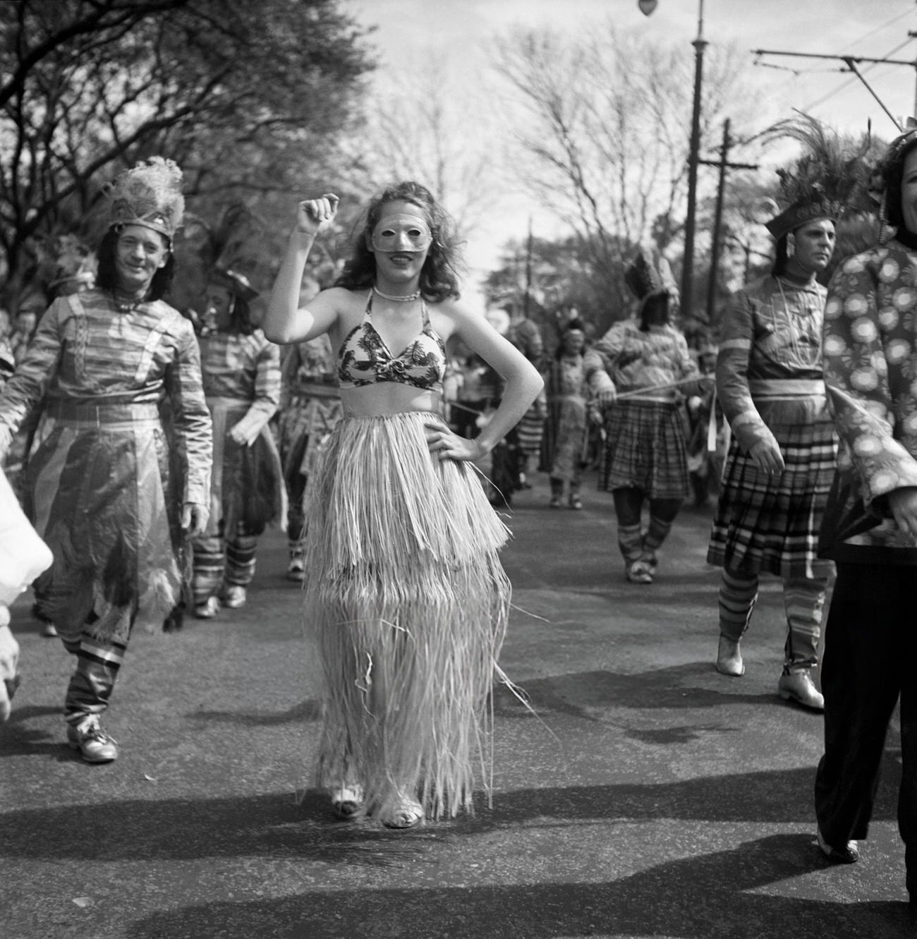 #42 A Woman Dances in a Hula Skirt in a Mardi Gras Parade Amidst Men in Costumes, 1950s.