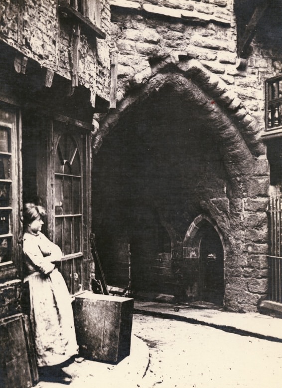 #3 Black Gate, close-up of the gateway with a woman leaning against a shop doorway, 1880.
