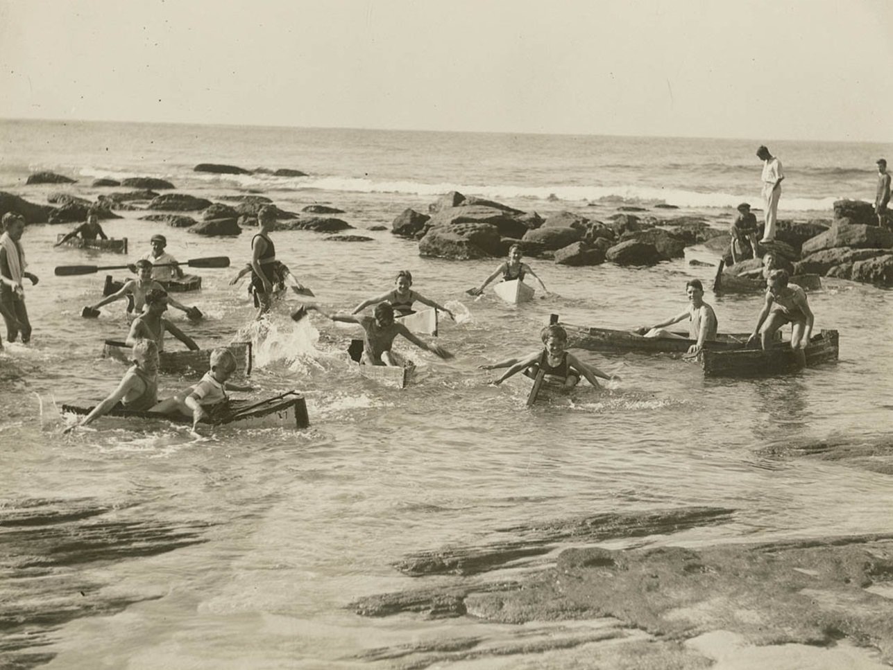 #41 Men and boys swimming and playing in canoes in a beach rock pool.